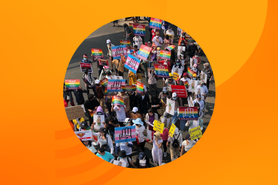 A crowd marches in Myanmar with rainbow flag and trans flag signs reading #LGBTQ4Democracy