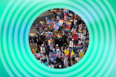 A crowd marches in Myanmar with rainbow flag and trans flag signs reading #LGBTQ4Democracy