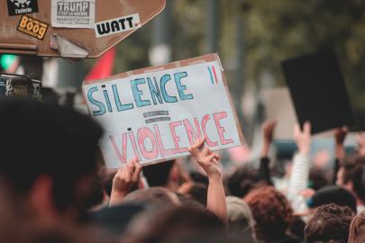 Person holding a sign that says, "Silence Equals Violence"