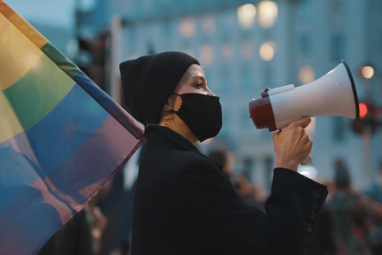 person with rainbow flag and megaphone wearing a face mask