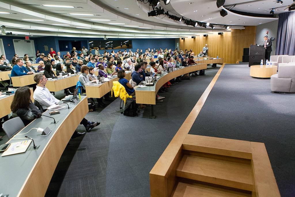 People sitting in rows, facing a stage with a speaker at a podium